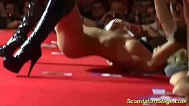 Busty milf stripping on stage with clothes ripped off in public.