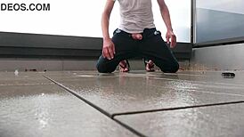 Masked figure masturbates outdoors in wet jeans on a rainy balcony.