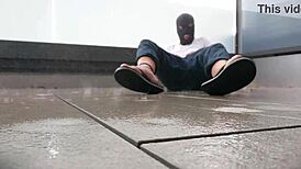 Masked figure masturbates outdoors in wet jeans on a rainy balcony.